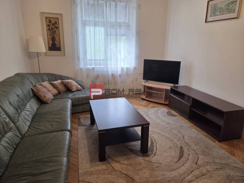 Obývací pokoj s rohovou sedačkou, televizí a konferenčním stolkem v 2pokojovém bytě.