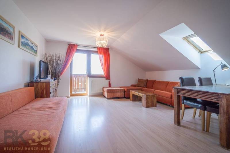 Rekreační apartmán s oranžovou sedací soupravou a jídelním stolem pod střešním oknem.