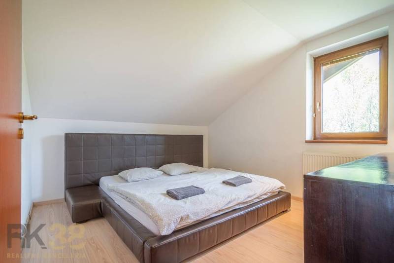 Ložnice v rekreačním apartmánu s manželskou postelí, oknem, dřevěným nábytkem a šikmými stropy.