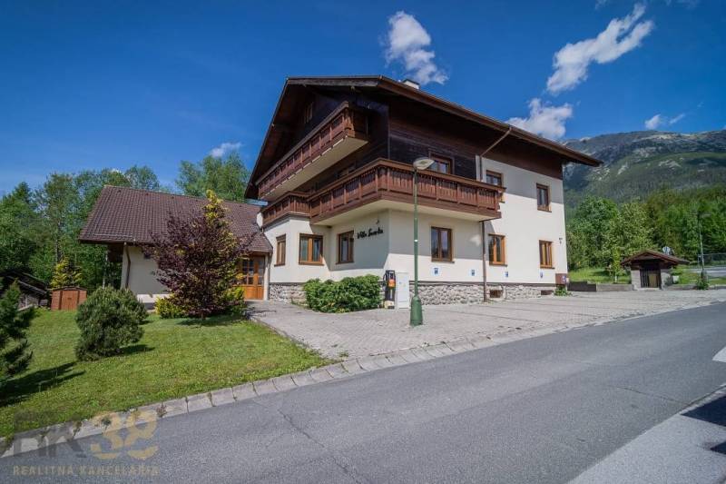 Rekreační apartmán ve Vysokých Tatrách, obklopený zelení, modrá obloha, hory v pozadí.