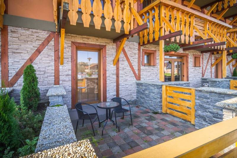 Kamenná terasa Rekreačního apartmánu ve Velké Lomnici s dřevěným zábradlím a stolkem.