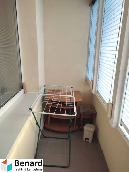 Zasklený balkon v 2-pokojovém bytě s poličkou, sušákem a odpadkovým košem.