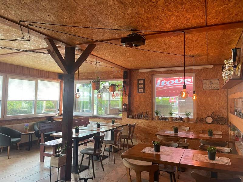 Interiér gastro prostorů se stoly, dřevěným obložením a dekorativními světly.