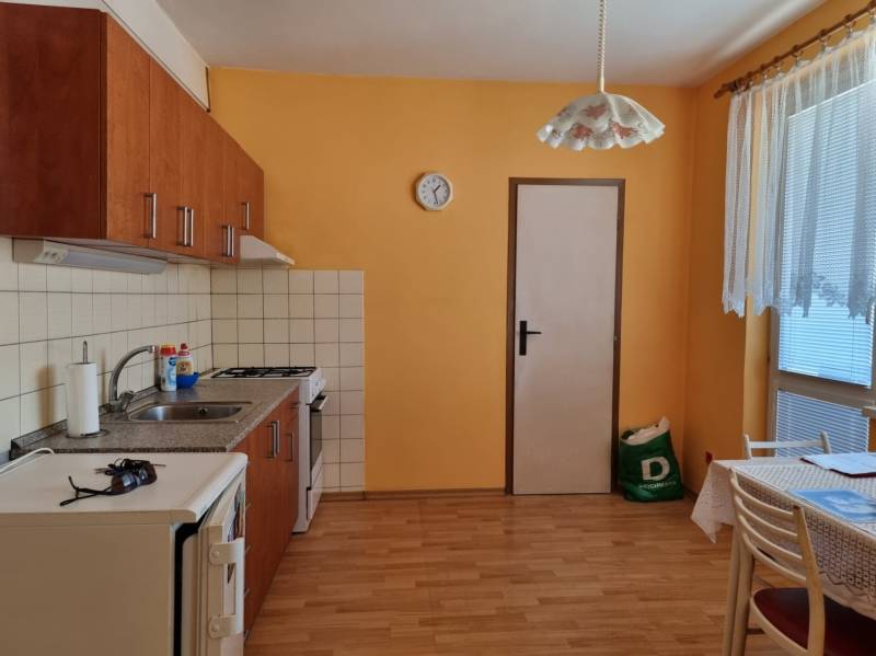 Kuchyně v 2-pokojovém bytě s oranžovými stěnami, dřevěnou podlahou a jídelním stolem.