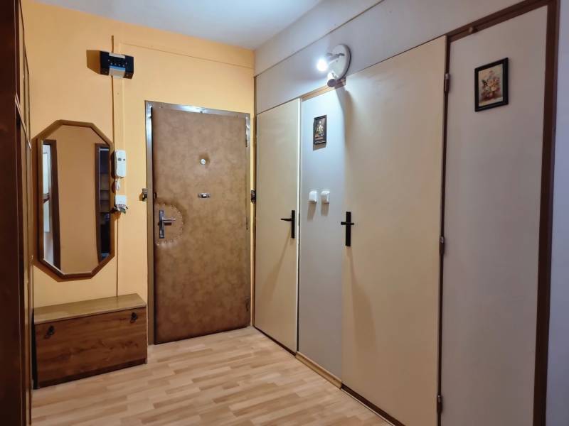 Chodba v 2-pokojovém bytě s dřevěným nábytkem, zrcadlem a bezpečnostními dveřmi.