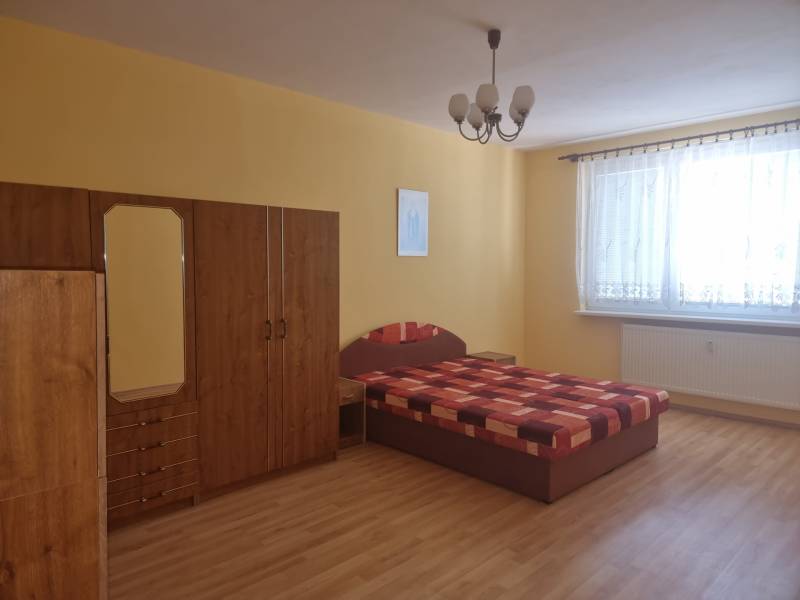 Ložnice v dvoupokojovém bytě s postelí, šatní skříní a žlutými stěnami.