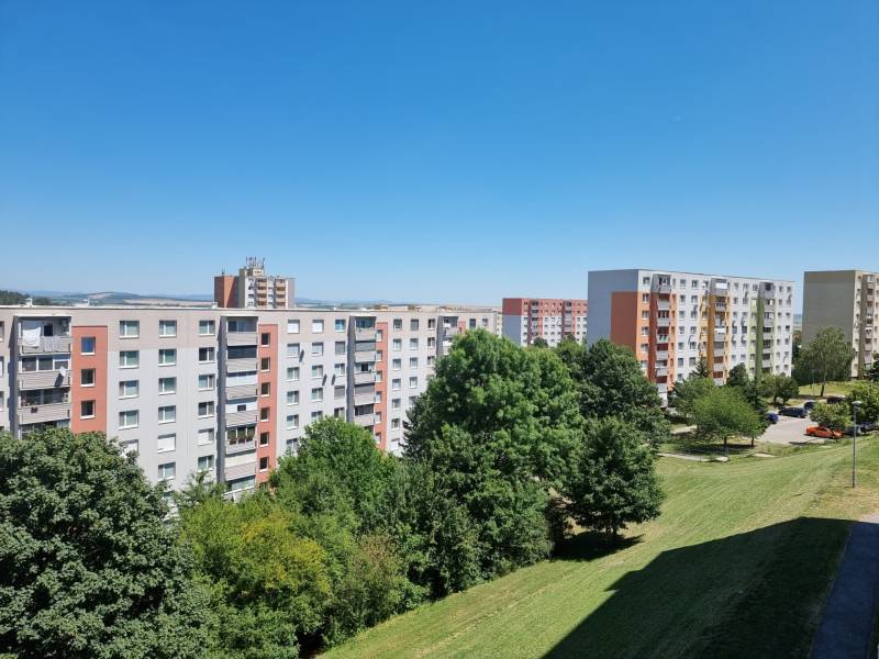 Sídliště s paneláky na Petzwalově ulici v Nitře, obklopené zelení a modrou oblohou.