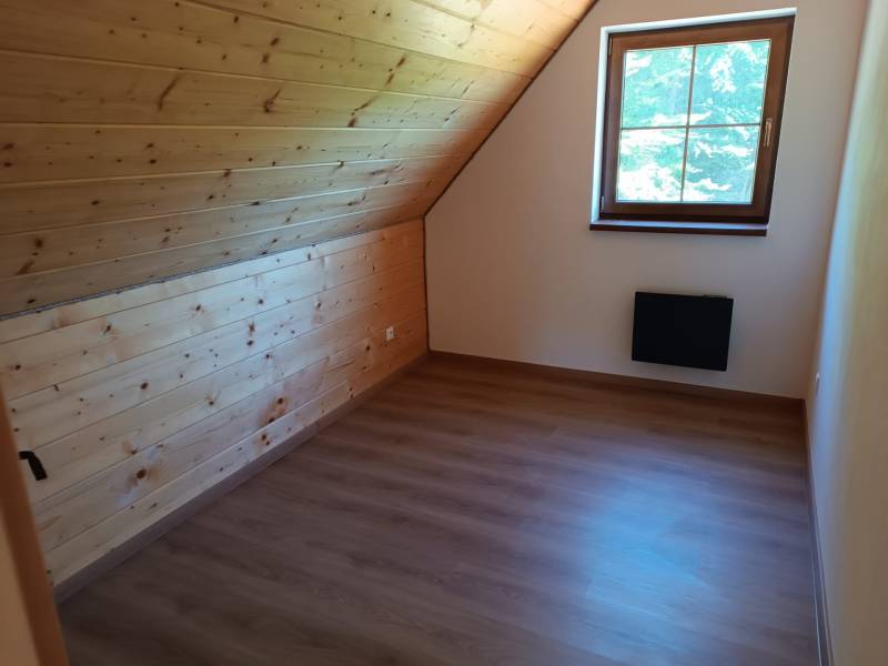 Podkrovní pokoj s dřevěným obložením a výhledem z okna na chatě.