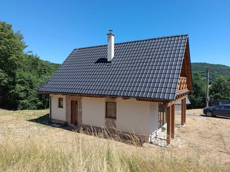 Chata v Horních Hamrech s dřevěnou střechou a verandou, obklopená přírodou.