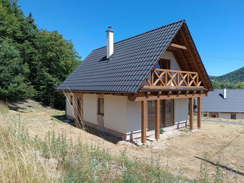Chata v Horních Hamrech s dřevěným balkónem, obklopená přírodou a svěží zelení.