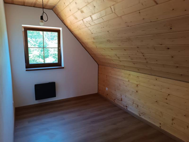 Podkrovní místnost s dřevěným obkladem, oknem a jednoduchým osvětlením v chatě.