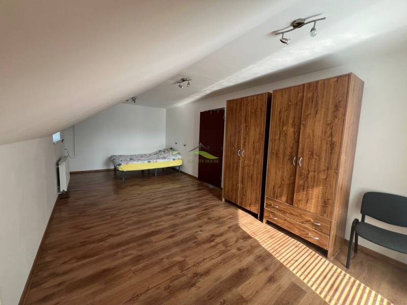 Podkrovní pokoj v rodinném domě s postelí, skříněmi a dřevěnou podlahou.