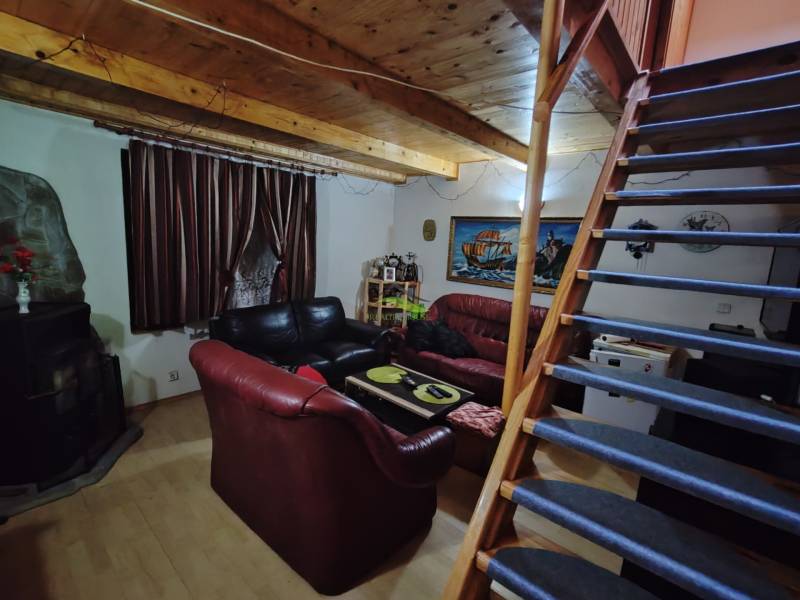 Interiér chaty s dřevěným stropem, pohovkami a schodištěm vedoucím do patra.