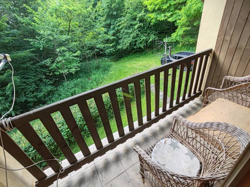 Balkon chaty s proutěnými židlemi a výhledem na zahradu a zeleň.