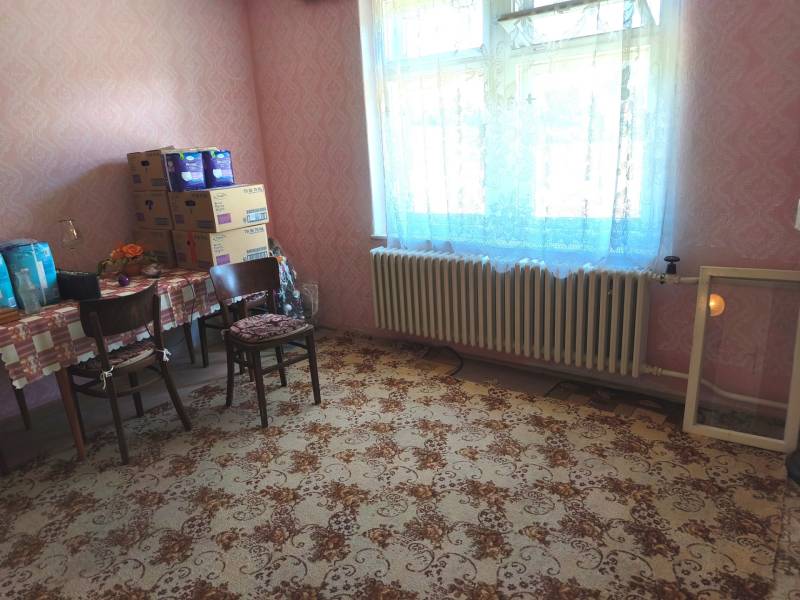 Pokoj v rodinném domě s kobercovým vzorem a stolem se židlemi.
