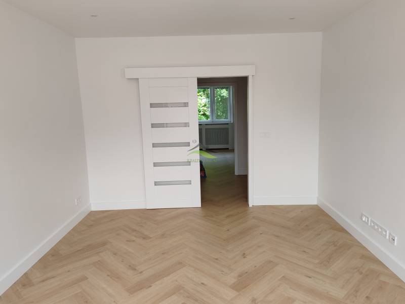 Pokoj v 2pokojovém bytě s dřevěnou podlahou a posuvnými bílými dveřmi.