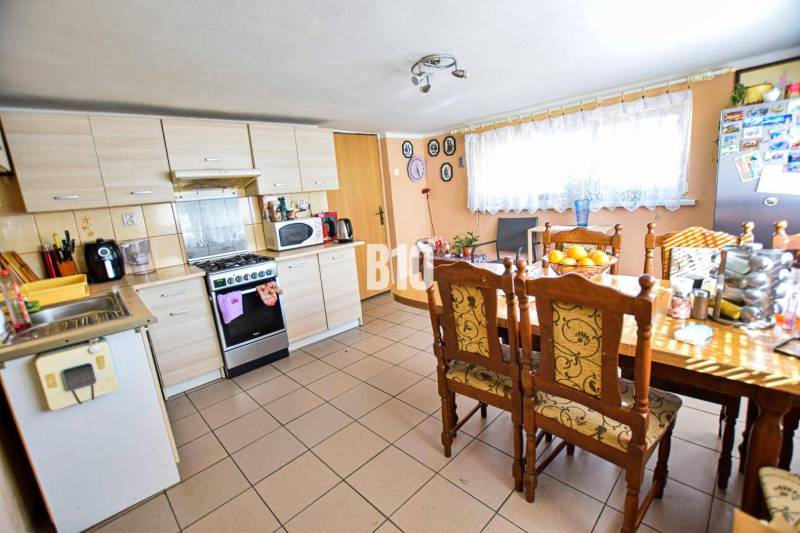 Kuchyně v rodinném domě s velkým stolem, dřevěnými židlemi a spotřebiči.