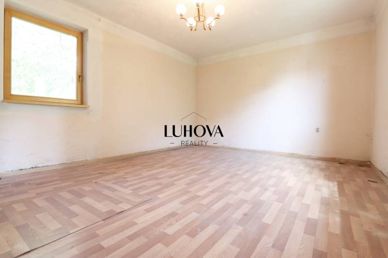 Prázdná místnost s dřevěnou podlahou a oknem v rodinném domě, neutrální stěny.