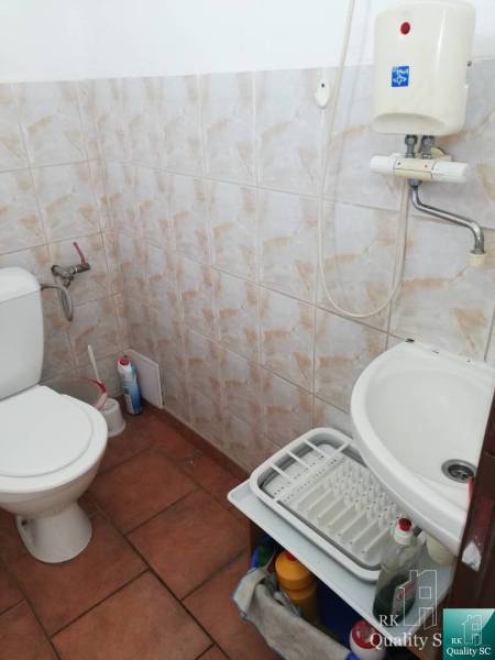 Koupelna v kancelářích s toaletou, umyvadlem a čisticími potřebami.