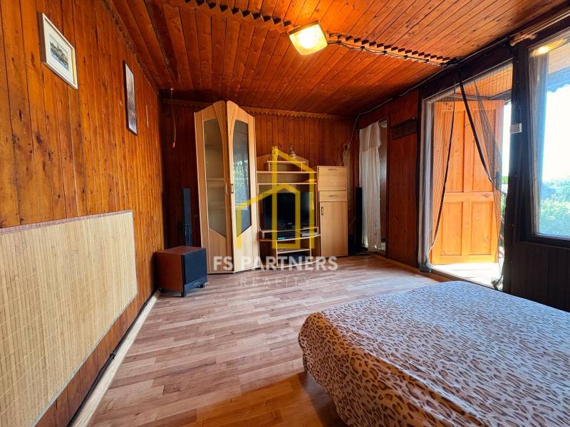 Dřevěný interiér s postelí a skříní, označený logem realitní kanceláře.