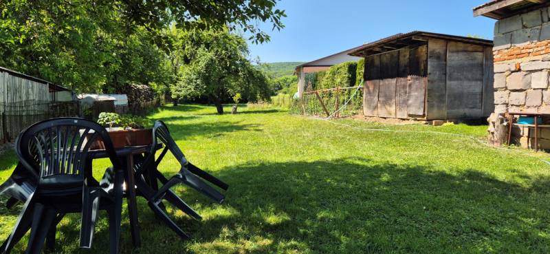 Zahrada rodinného domu ve Slovenské Kajni s plastovými židlemi a dřevěným přístřeškem.