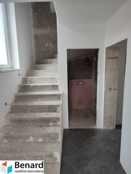 Schodiště a nedokončená koupelna v rodinném domě s šedou dlažbou a bílými stěnami.