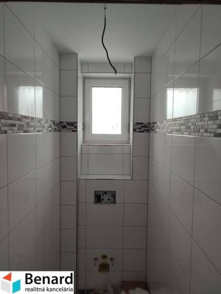Koupelna v rodinném domě s obkladem a oknem, bez sanitárního vybavení.