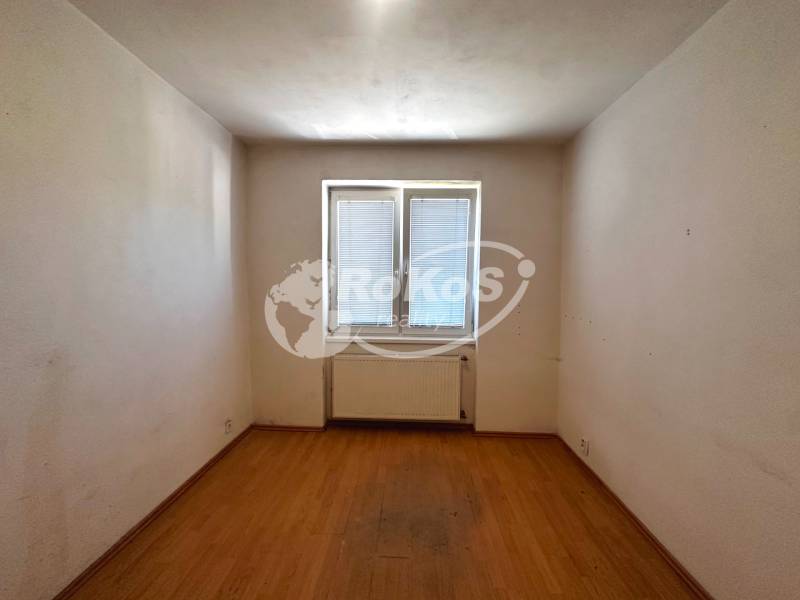 Prázdný pokoj s parketovou podlahou a oknem ve 3pokojovém bytě.