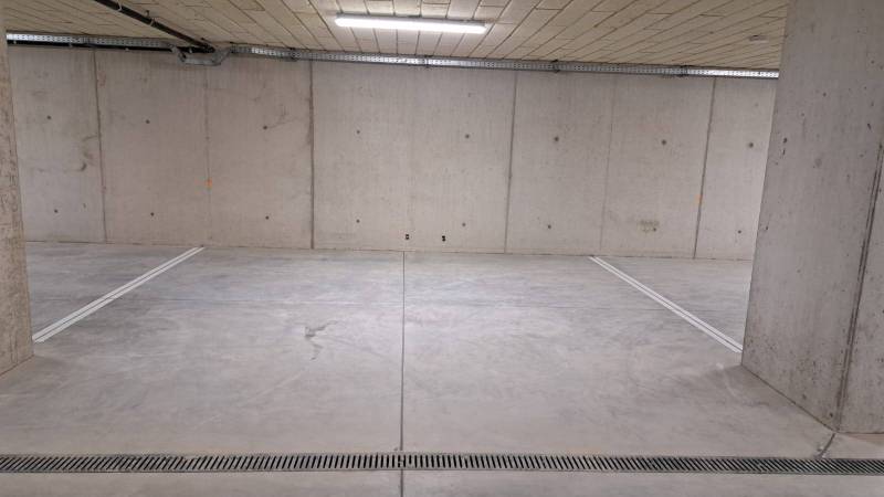 Parkovací místo v podzemní garáži s betonovými stěnami a podlahou.