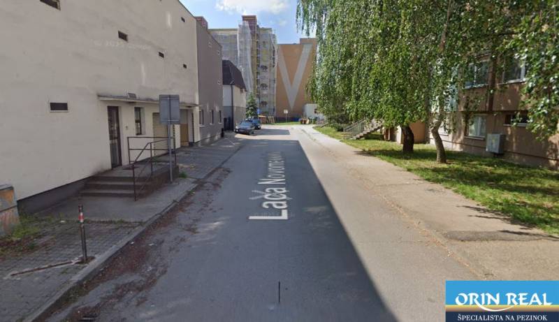 Ulice L. Novomeského v Pezinku s garážemi, obytnými domy a zelení.