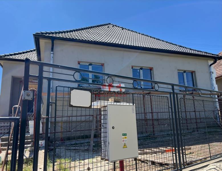 Rodinný dům v Sasinkově na ulici Sasinkovo s nedokončenou fasádou za kovovým plotem.