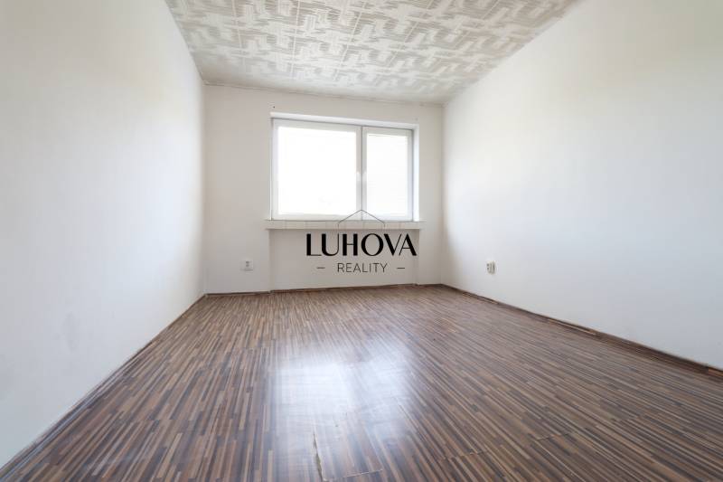 Prázdný pokoj s dřevěnou podlahou a bílým stropem v dvoupokojovém bytě.