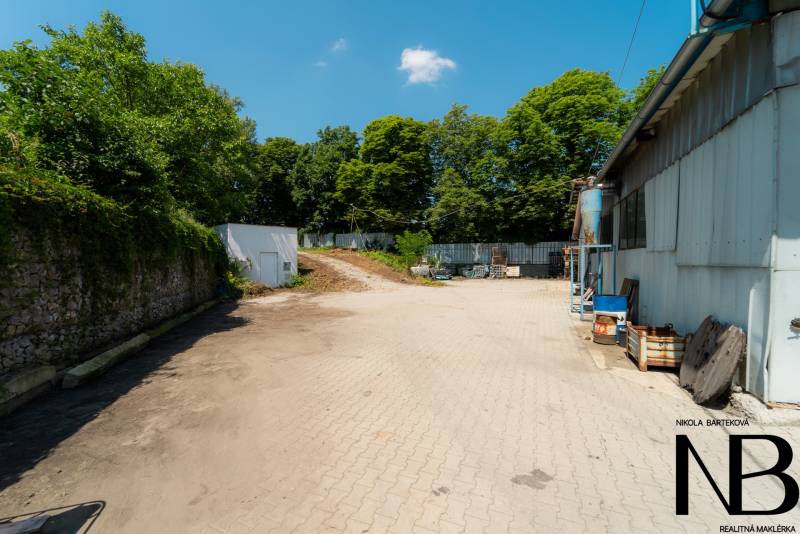 Zpevněná plocha u skladové haly na Kasárenské ulici v Trenčíně obklopená zelení.