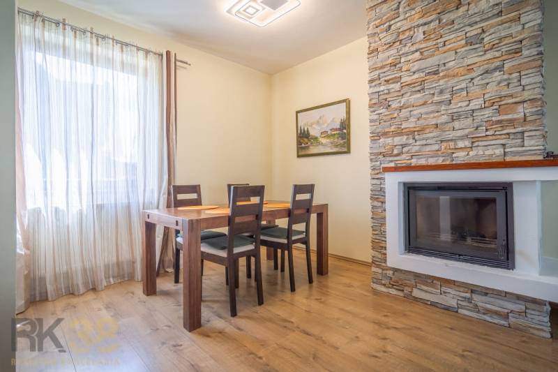 Jídelna v rekreačním apartmánu s dřevěným stolem a krbem obloženým kamenem.