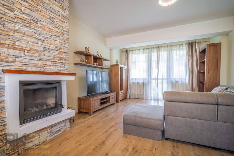 Obývací pokoj v rekreačním apartmánu s krbem, gaučem a velkým oknem.