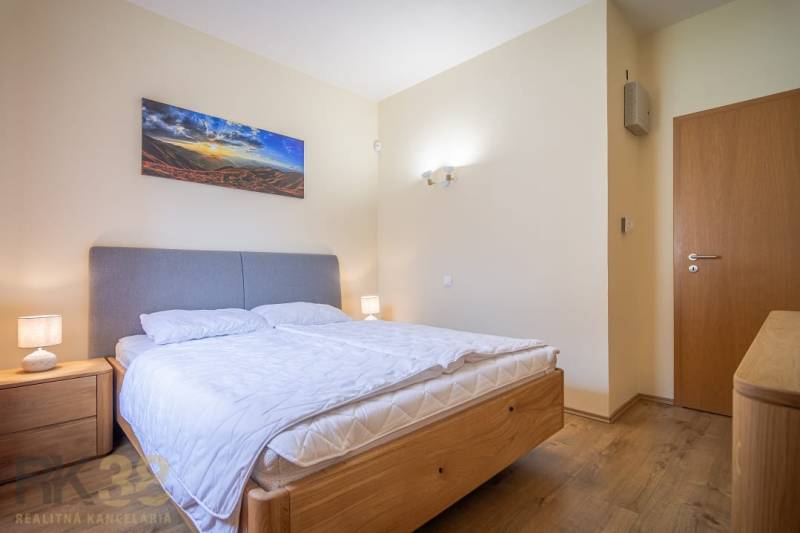Světlá ložnice rekreačního apartmánu s manželskou postelí, nočními stolky a dekorací na stěně.
