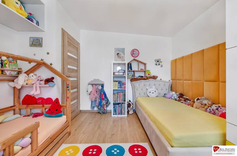 Dětský pokoj v rodinném domě s postelemi, poličkami a hračkami, světlé dřevěné podlahy.