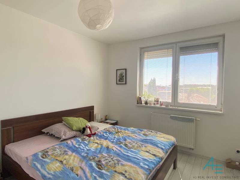 Ložnice ve 3pokojovém bytě se slunečním oknem, velkou postelí a pokojovými rostlinami.