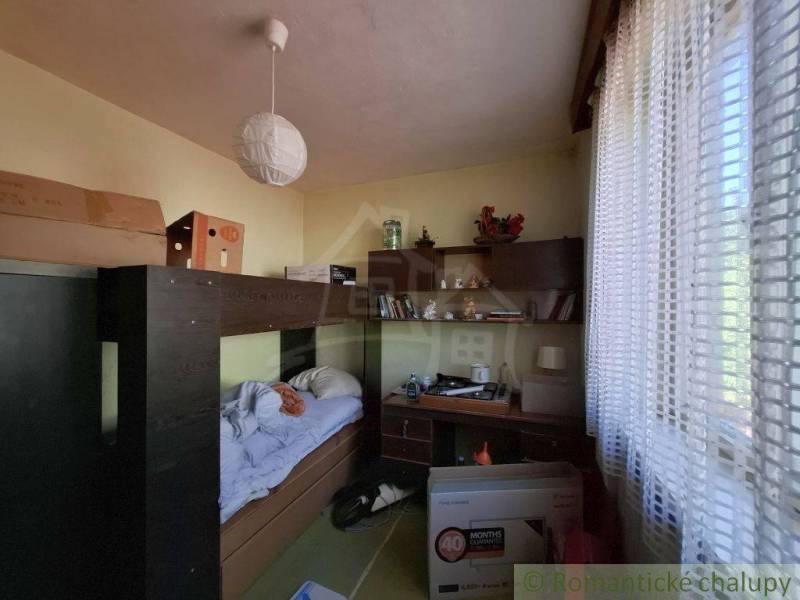 Pokoj v rodinném domě s postelí, stolem a regálem.