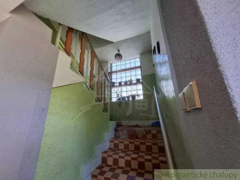 Schodiště v rodinném domě s květinami na okně a zábradlím.