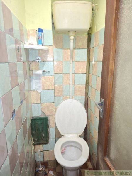 Jednoduchá koupelna v rodinném domě se starší toaletou a dlaždičkami.