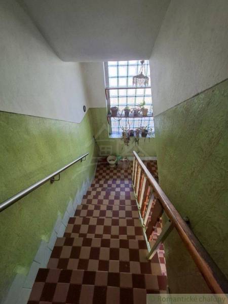 Schodiště v rodinném domě se zelenými stěnami a šachovnicovou dlažbou.