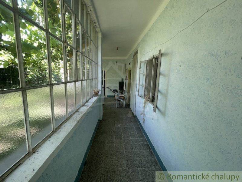 Zasklená veranda v rodinném domě s výhledem na zahradu a nábytkem.