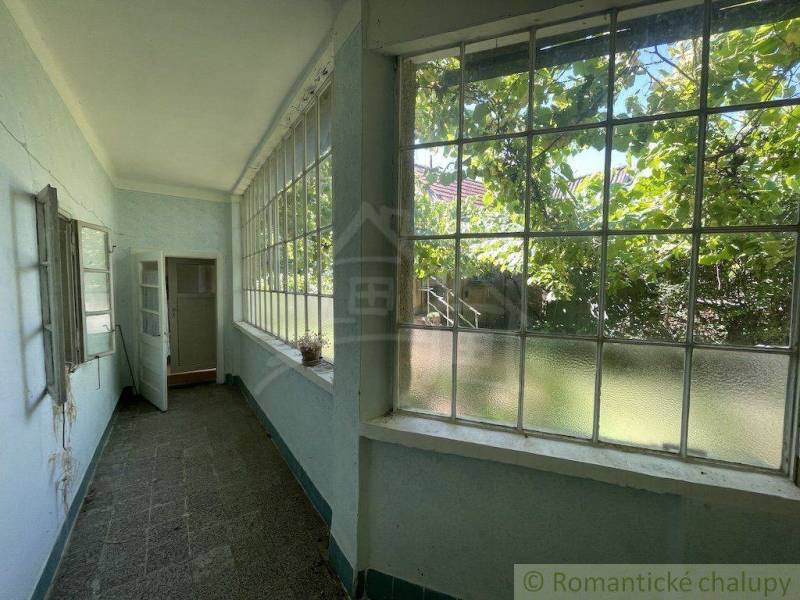 Světlá veranda rodinného domu s velkými okny a výhledem na zahradu.