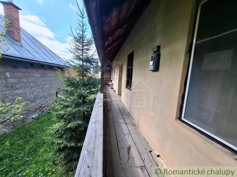 Dřevěný chodník vedle rodinného domu v Pohorelé, obklopený zelení a sousední budovou.