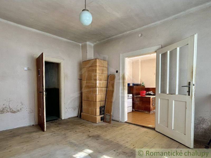 Pokoj s kachlovými kamny, dřevěnou podlahou a kuchyní v rodinném domě.