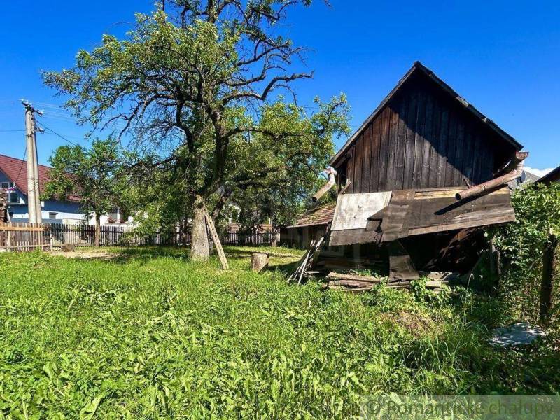 Zahrada v Gemerské Polomě u rodinného domu, s dřevěnou stavbou a velkým stromem.