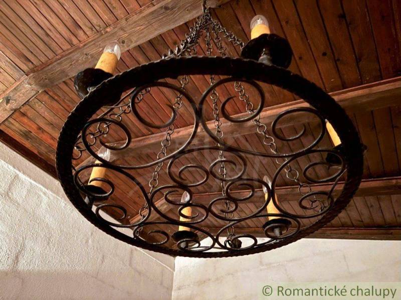 Kovaná lampa se svíčkami v interiéru rodinného domu s dřevěným stropem.