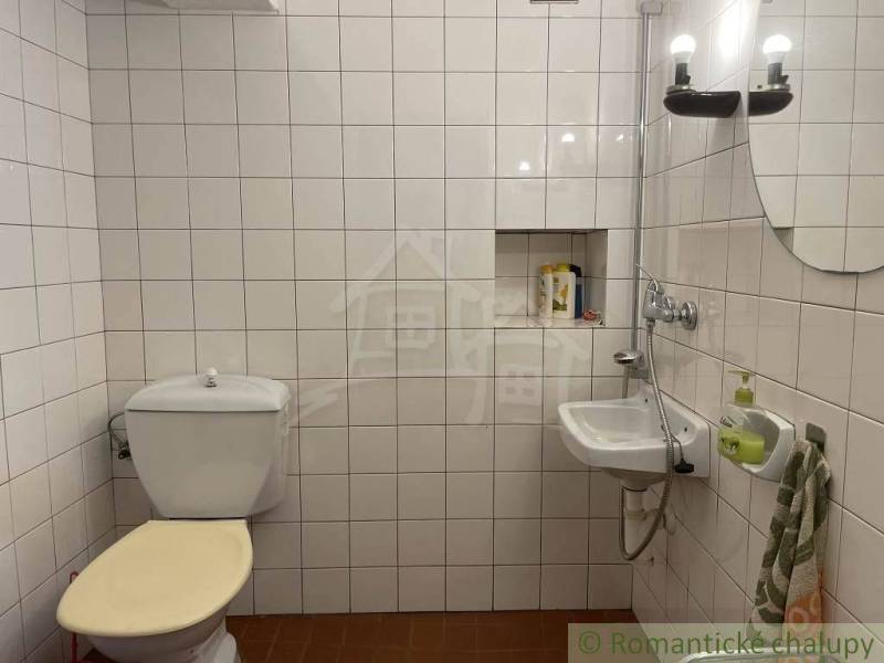 Koupelna se záchodem, umyvadlem, světly a bílými kachličkami, zvláštní nemovitosti.