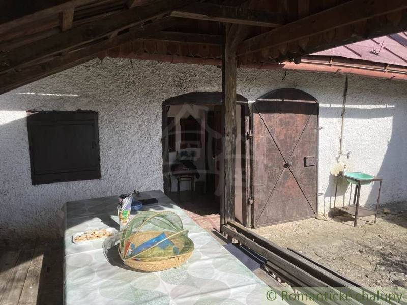 Veranda s dřevěnými dveřmi u chaty v Rožňavě se stolem a košíkem.